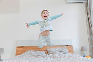Happy little boy jumping on bed